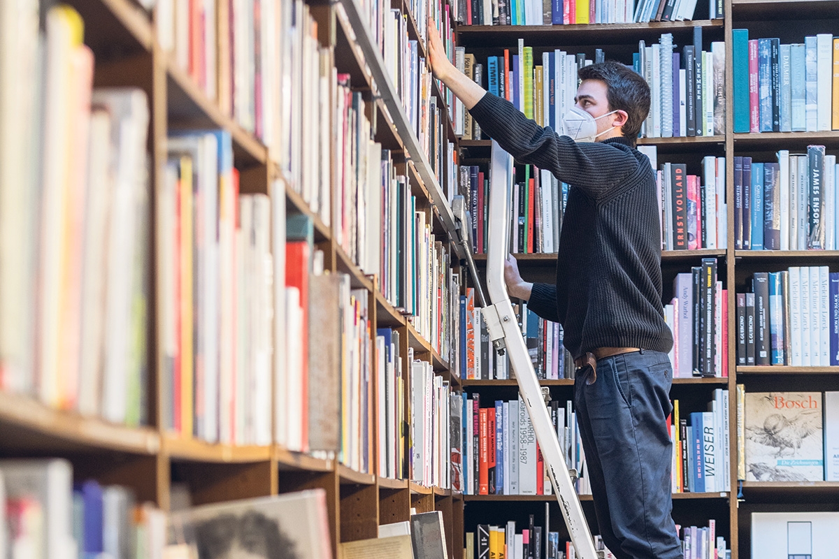 Mitarbeiter einer Buchhandlung der Walther-König-Kette steht auf einer Leiter vor einem großen Bücherregal