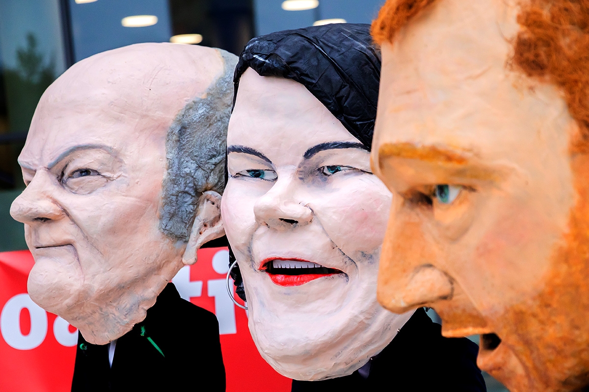 Drei Personen tragen Masken von Olaf Scholz, Annalena Baerbock und Christian Lindner