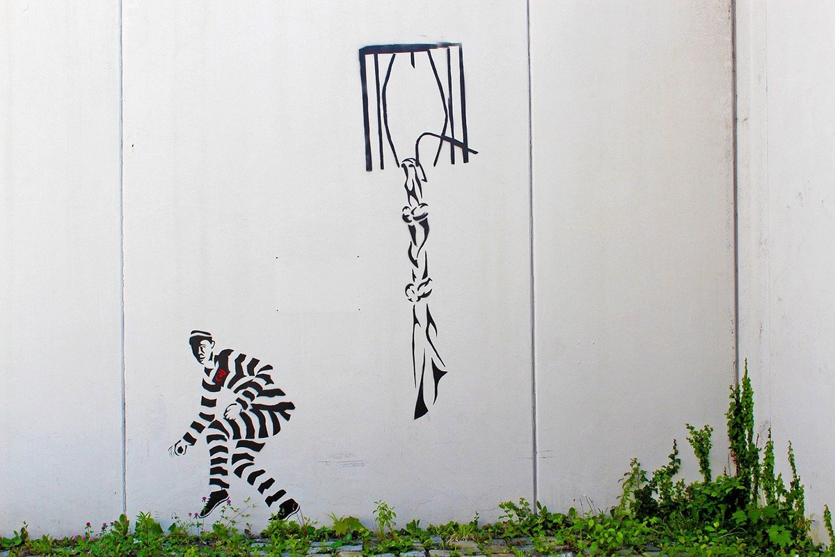 Graffiti Knastmauer auf einer Knastmauer: Fenster mit geknotetem Laken und Person in Knastkleidung, die wegschleicht