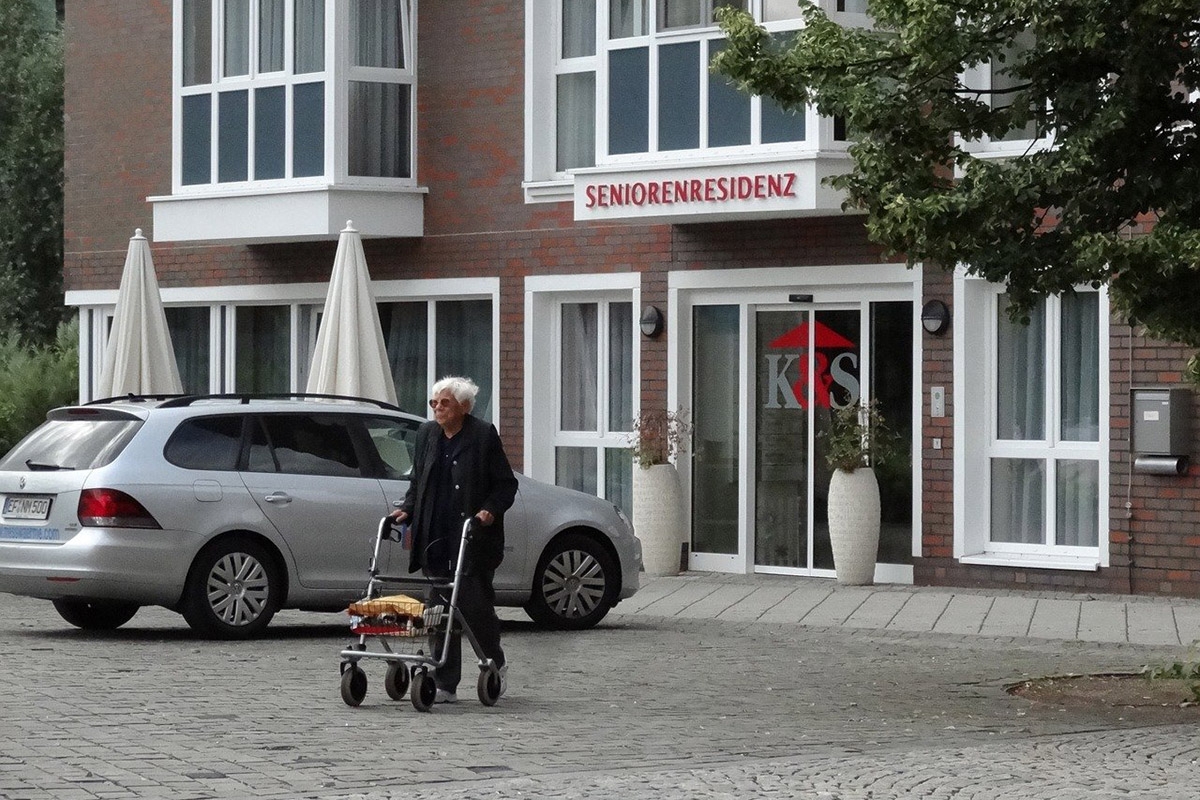 Person mit Rollator vor einem Haus mit Aufschrift Seniorenresidenz