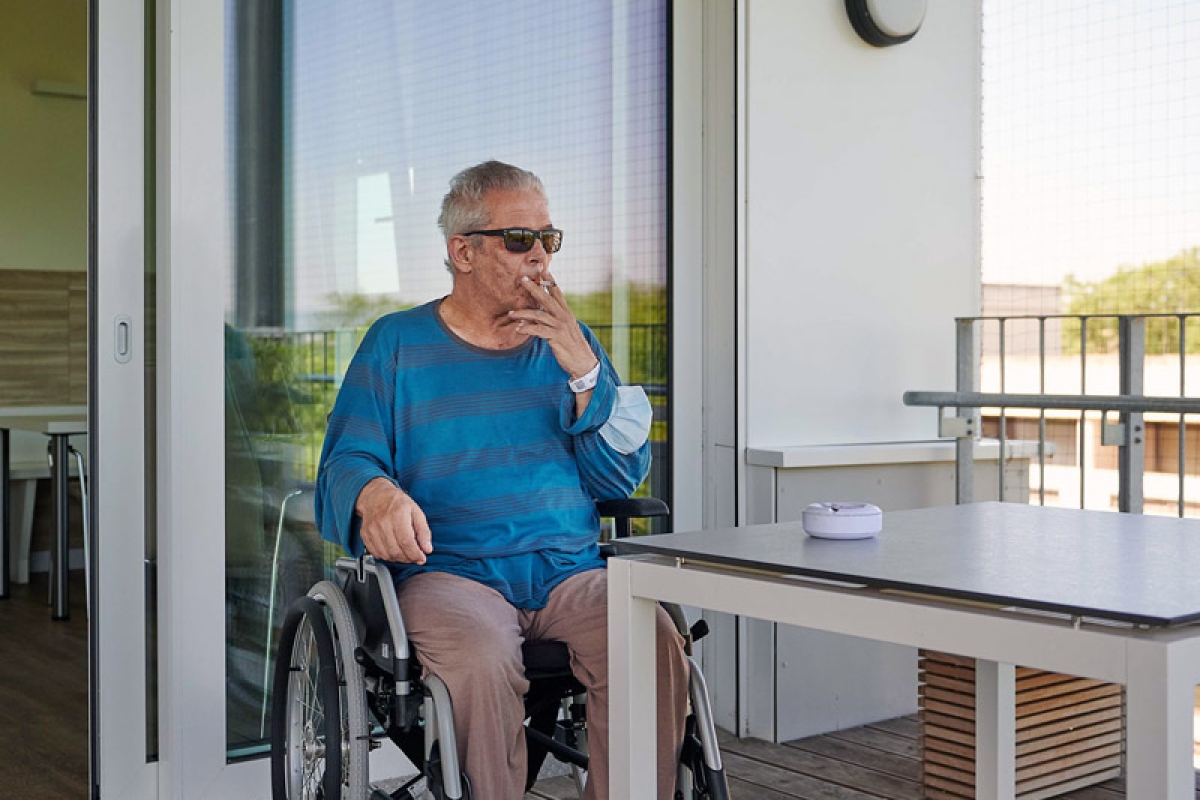 Ein Mann im Rollstuhl raucht auf einem Balkon