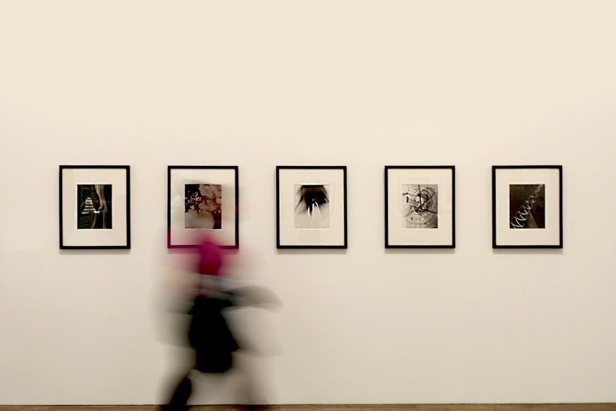 Eine Person läuft in einer Ausstellung an vier Bildern vorbei