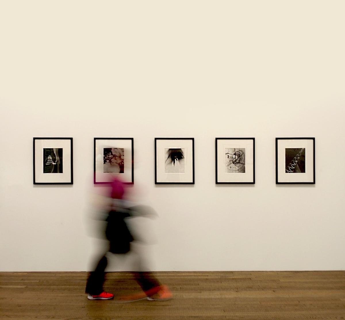 Eine Person läuft in einer Ausstellung an vier Bildern vorbei