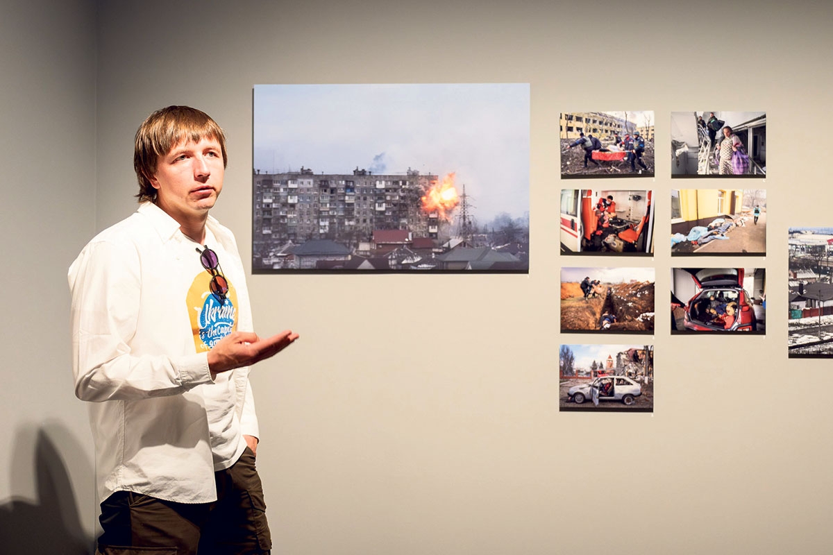 Evgeniy Maloletka neben seinen Bildern, die er in Mariupol im März 2022 aufnahm