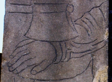 Auf einem Stein eingearbeitetes Motiv: eine Hand wird mit einem Beil abgeschlagen