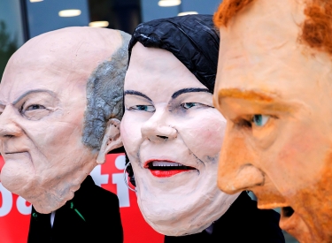Drei Personen tragen Masken von Olaf Scholz, Annalena Baerbock und Christian Lindner