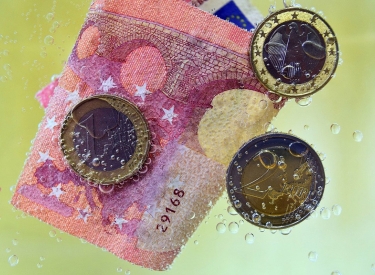 Geldschein und Münzen im Wasser mit Bläschen