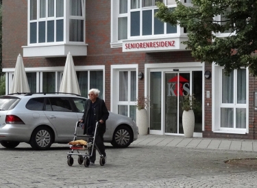 Person mit Rollator vor einem Haus mit Aufschrift Seniorenresidenz