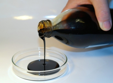 Eine braune zähflüssige Substanz wird aus einer Glasflasche in ein Schälchen gegossen