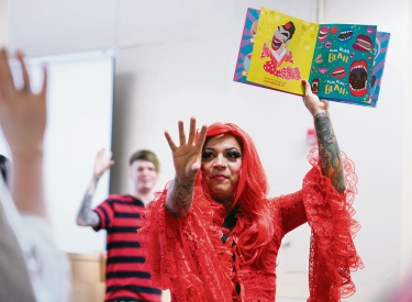 Drag Queen hält ein Kinderbuch hoch auf dem Blah Blah steht