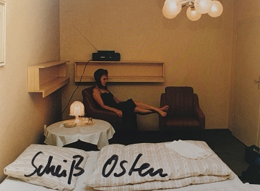 Foto einer Frau in einem Hotelzimmer, beschriftet mit »Scheiß-Osten«