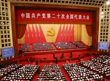 Ein mit roten Fahnen geschmückter Konferenzsaal voller Menschen