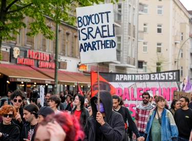 Demonstrant bei der Revolutionären 1.-Mai-Demonstration in Berlin mit Schild "Boycott Israeli Apartheid"eder israelfeindliche Schilder am Start