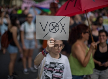 Demonstrantin mit Schild, auf dem"Vox" durchgestrichen und im O von Vox ein Hakenkreuz zu sehen ist