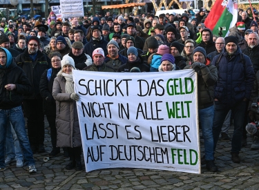 Teilnehmer der Kundgebung auf dem Domplatz halten ein Transparent mit der Aufschrift "Schickt das Geld nicht in alle Welt, lasst es lieber auf deutschem Feld". 
